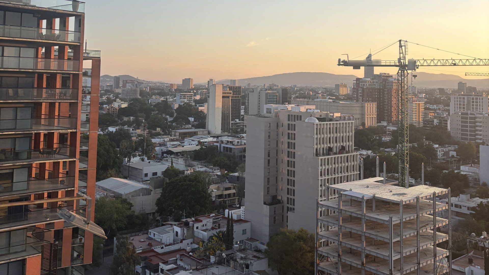 Panorámica de una ciudad al atardecer con grúa torre y edificios en construcción